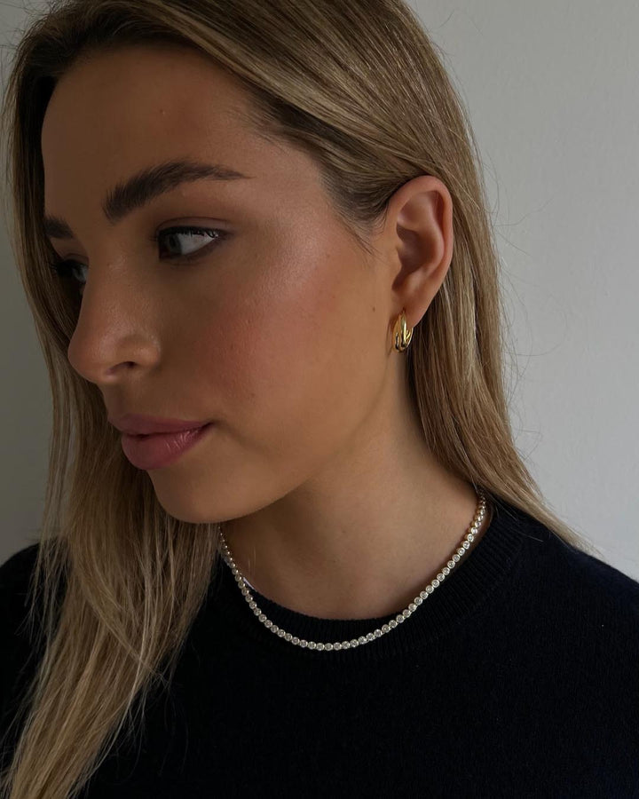 model wearing gold tennis necklace and gold hoop earrings