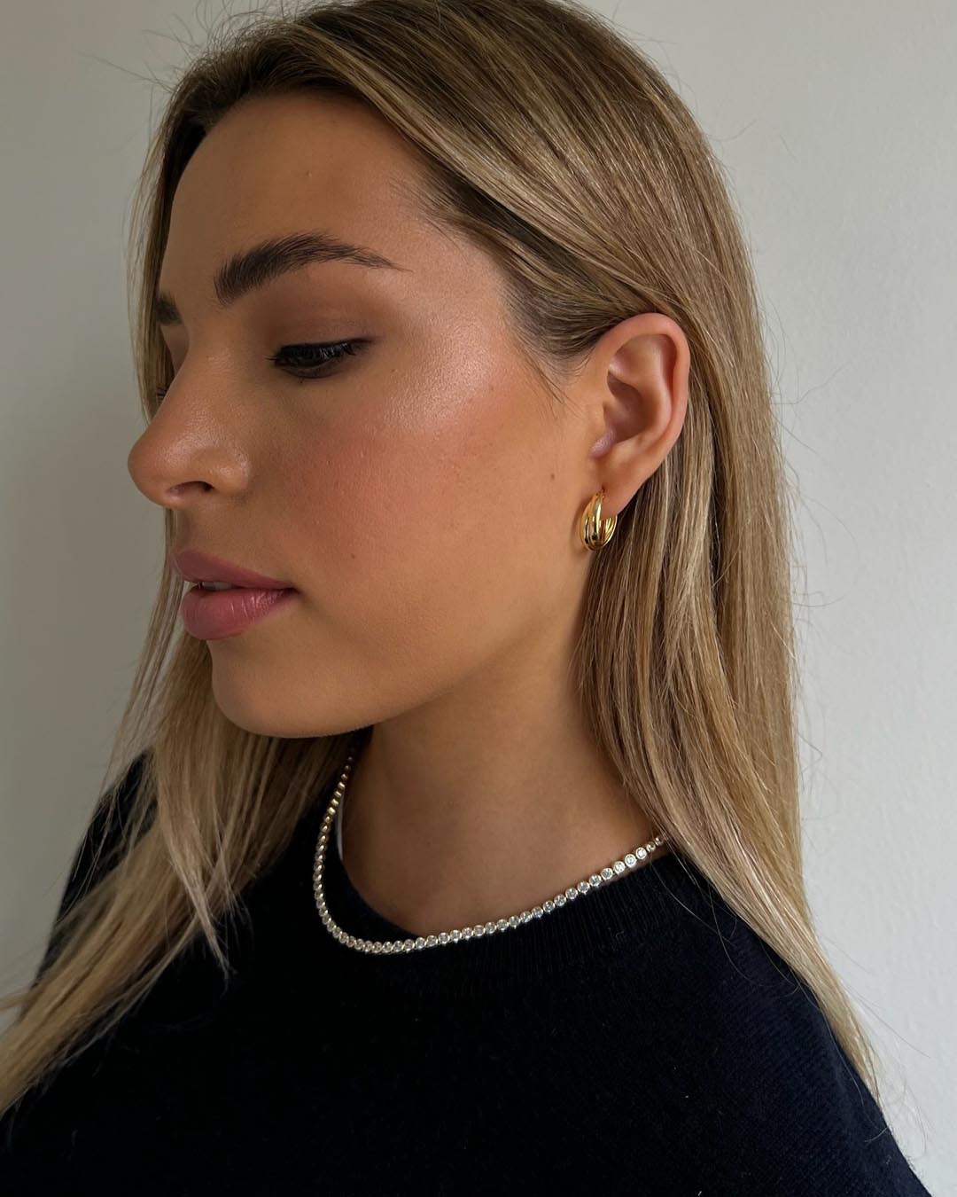 model wearing gold tennis necklace and gold hoop earrings