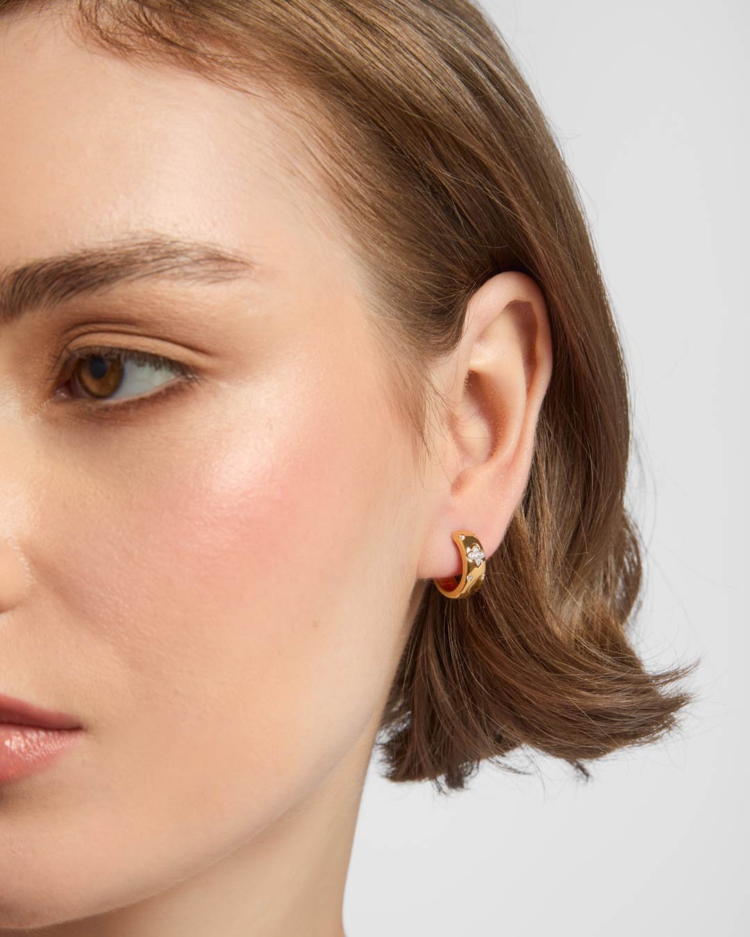 model wearing gold plated clover huggie earrings
