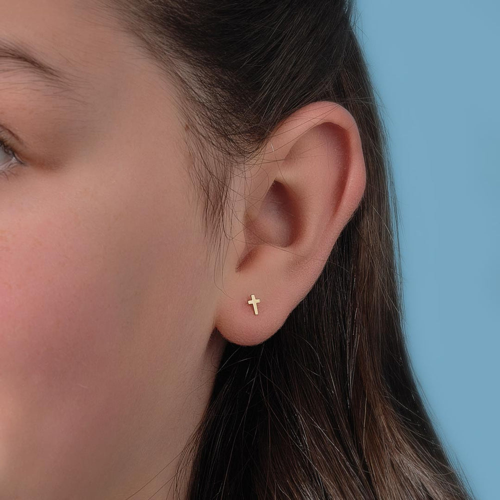 model wearing tiny cross stud earrings in yellow gold