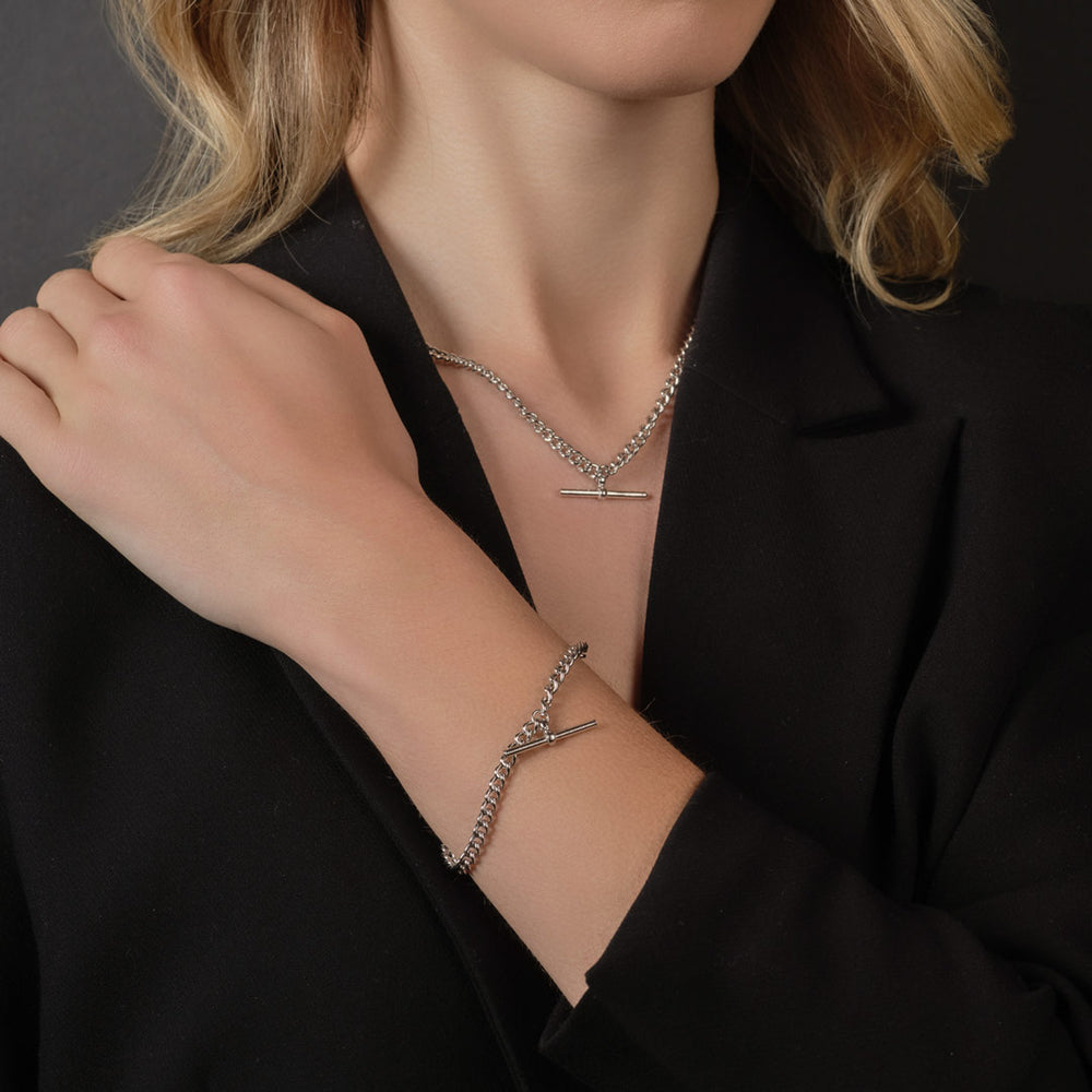 The photo features a close-up shot of a female model showcasing a matching silver T-bar pendant and bracelet set against a dark background.